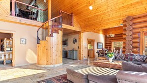 A spacious log cabin interior with a central staircase, a cozy seating area, and a dining space.