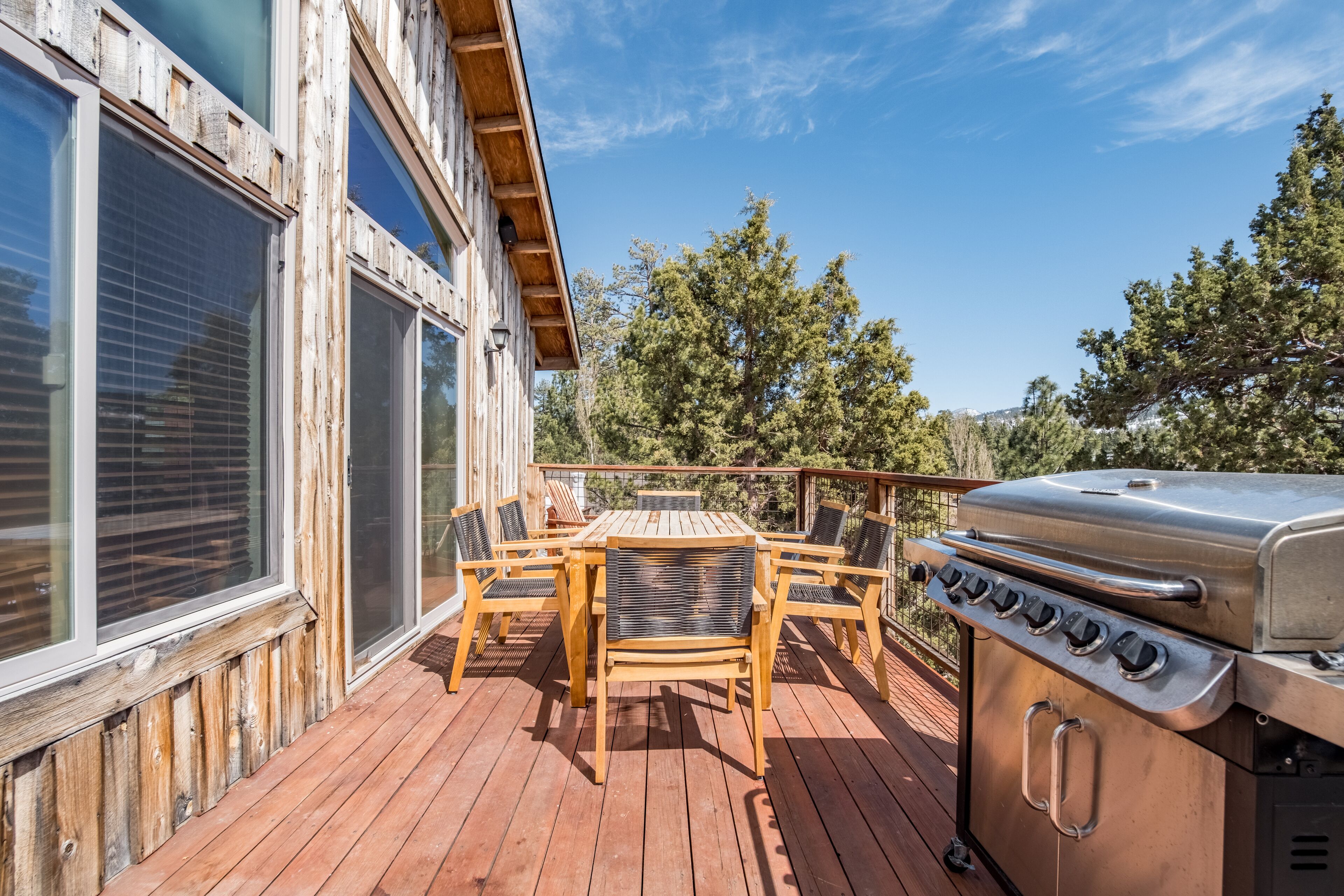 A wooden deck with a grill and chairs, overlooking a forested area.