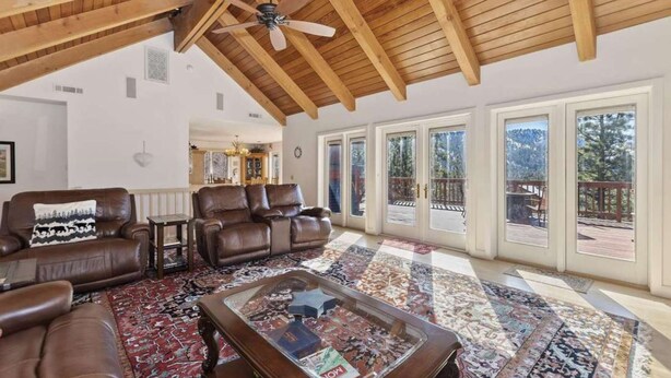 A spacious living room with leather sofas, a coffee table, and a large window overlooking a deck. - Views at Wolf Lodge by AvantStay | Magnificent Views w/ Hot Tub, Sauna, Games (Big Bear Lake)