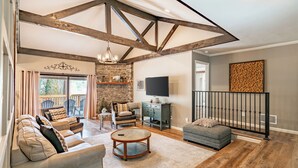 A spacious living room with a stone fireplace, a large sofa, a round coffee table, and a television.