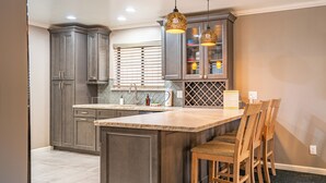 A kitchen with dark gray cabinets, a large island with bar stools, and pendant lighting.