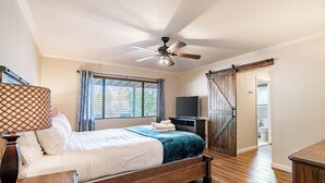 A bedroom with a bed, a ceiling fan, a TV, and a sliding door leading to a bathroom.