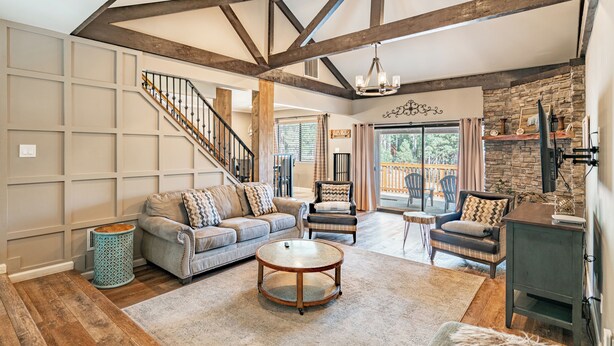 A spacious living room with a high ceiling, exposed beams, a fireplace, and a staircase leading to another level.