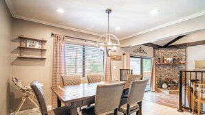 A dining area with a wooden table and chairs, a hanging light fixture, and a stone fireplace.