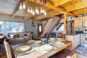 A wooden dining table set with plates and a rustic kitchen with wooden cabinets and a stove. - 50 yards to Lake, Boulder Bay • Pool Table | Lakeside in Bearadise by AvantStay (Big Bear Lake)