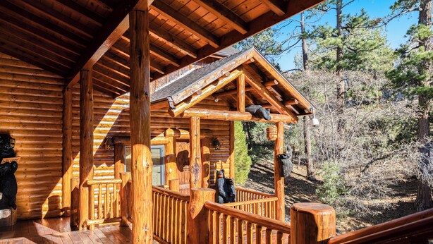 A wooden log cabin with a porch, wooden railings, and a view of a forested hillside.