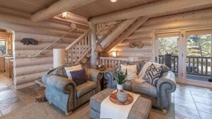 L'intérieur d'une cabane en rondins, avec un escalier, deux canapés, une table basse et une vue à travers une porte vitrée.