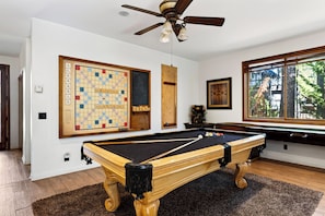 A pool table with a wooden finish, a ceiling fan, and a large chessboard on the wall. - Walk to Lake | 6BR Cabin w/ Game Room, Hot Tub | Big Bear Castle (Big Bear Lake)