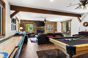 Een ruime woonkamer met een pooltafel, comfortabele zitplaatsen, een open haard en grote ramen.