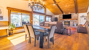 Een ruime woonkamer met een houten plafond, een open haard en een eettafel met stoelen.