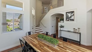 A dining area with a wooden table and chairs, a staircase, and a view of the outdoors.