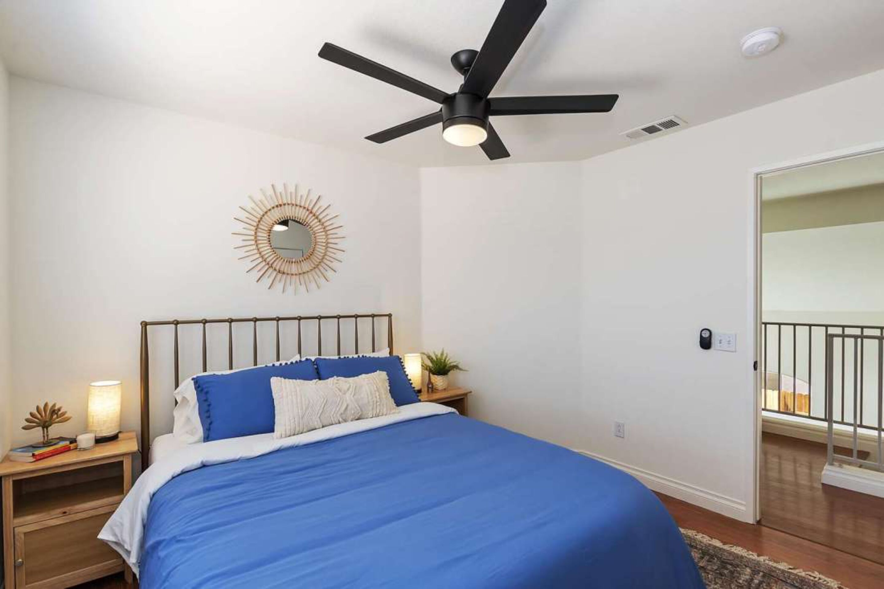 A bedroom with a bed, a ceiling fan, a nightstand, a wall clock, and a door to a balcony.