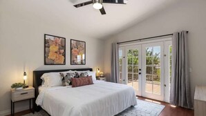 A bedroom with a large bed, a ceiling fan, two wall-mounted lamps, and a sliding glass door leading to an outdoor area.