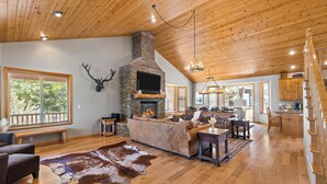 A spacious living area with a fireplace, wooden ceiling, and large windows.