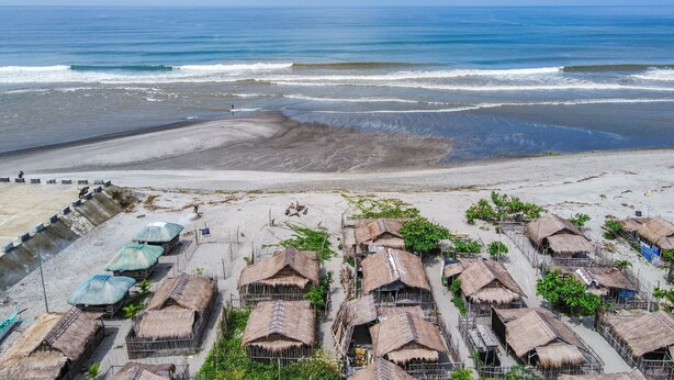 Un village côtier avec des huttes aux toits de chaume et une plage en arrière-plan.