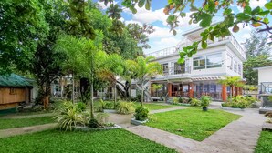 Une cour avec une pelouse bien entretenue, un arbre au centre et un bâtiment doté d’un balcon et d’un espace extérieur aménagé pour s’asseoir.