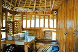 A wooden interior with a thatched roof, a wooden bench, and a table with water bottles. - Youhan Beach Resort powered by Cocotel (San Antonio)