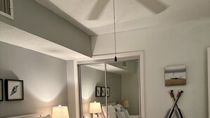 Un dormitorio con una cama grande, un ventilador de techo, un espejo y una mesita de noche con lámpara.