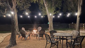 An outdoor seating area with a fire pit, string lights, and chairs.