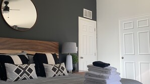 A bedroom with a bed, a ceiling fan, a round mirror, a door, and a stack of towels. - Entire Home! Big Style, Big Views, Great Location! (Pine)