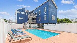 A two-story blue house with a swimming pool, a balcony, and a fenced patio area with lounge chairs.