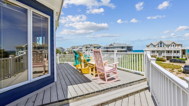 A wooden deck with outdoor furniture and a view of the ocean and beach houses.