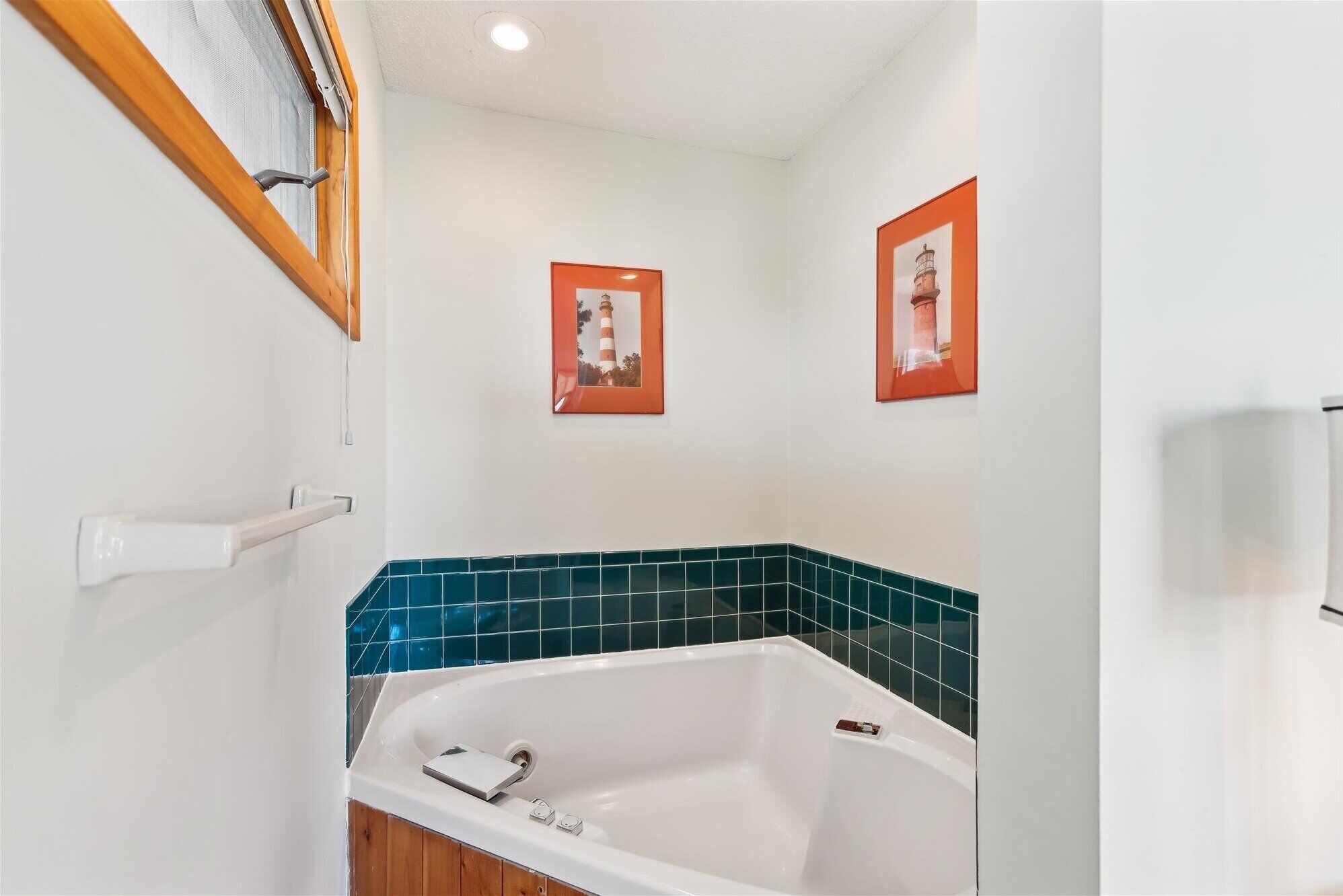A bathroom with a white bathtub, teal tiles, wooden paneling, and two framed pictures on the wall.