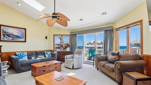 A spacious living room with a ceiling fan, large windows with ocean views, and a cozy seating area with a coffee table.