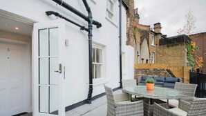 A white house with a glass door, a round glass table, wicker chairs, and a black fence in the background. - Modern Waterloo 1BR w/ open plan on Lower Marsh, by Blueground (London)