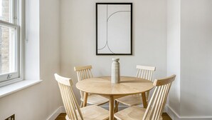 A dining area with a round wooden table and six chairs, a vase on the table, and a framed abstract artwork on the wall. - Modern Waterloo 2BR open plan with Balcony on Lower Marsh, by Blueground (London)
