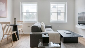 Una sala de estar moderna con un sofá gris, sillas de madera, una mesa de centro y un televisor sobre un mueble.