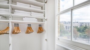 Un armario blanco con estantes y perchas de madera, un radiador y una ventana con vista a la ciudad.