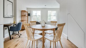 A modern room with a round wooden table, six wooden chairs, a desk with a chair, and a bookshelf. - Modern Waterloo 2BR open plan with Balcony on Lower Marsh, by Blueground (London)