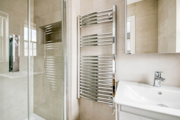 A modern bathroom with a glass shower enclosure, a chrome towel rack, and a white sink with a chrome faucet.