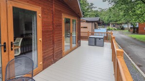 A wooden cabin with a porch, a dining table, and a chair. - Ridgway Lodge (Windermere)