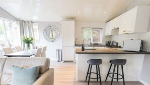 A modern kitchen with a central island, bar stools, and white cabinetry. - Buttermere Lodge (Windermere)