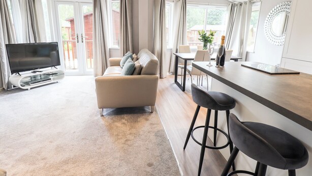 A modern living room with a sofa, a TV, and a dining area with a bar. - Buttermere Lodge (Windermere)
