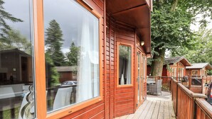 A wooden deck with a glass door leading to a room with a view of a car and trees. - Buttermere Lodge (Windermere)