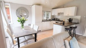 A modern kitchen with white cabinets, a dining area with a table and chairs, and a sofa with cushions. - Buttermere Lodge (Windermere)