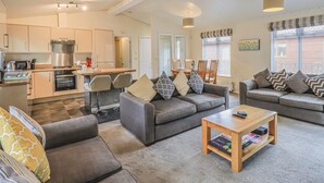 Ein modernes Wohnzimmer mit grauen Sofas, einem Couchtisch und einem Essbereich mit Küche im Hintergrund.