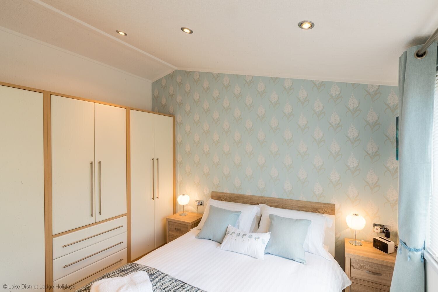 A bedroom with a bed, nightstands, a wardrobe, and a patterned wall.