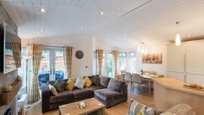 A spacious living area with a sofa, coffee table, and a dining area with chairs and a table. - Broad Larch Lodge (Windermere)