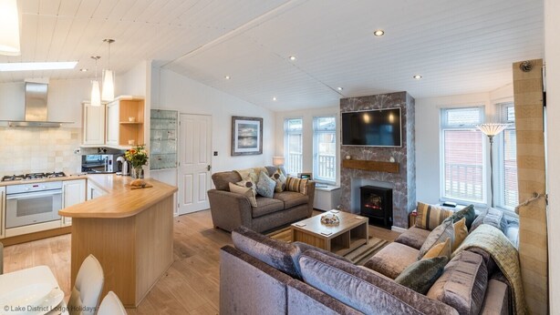 A spacious living area with a fireplace, a sofa, a coffee table, and a TV mounted on the wall. - Broad Larch Lodge (Windermere)