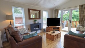 A living room with a brown leather sofa, a wooden coffee table, and a flat-screen TV on a wooden stand. - Wansfell Retreat Lodge (Windermere)