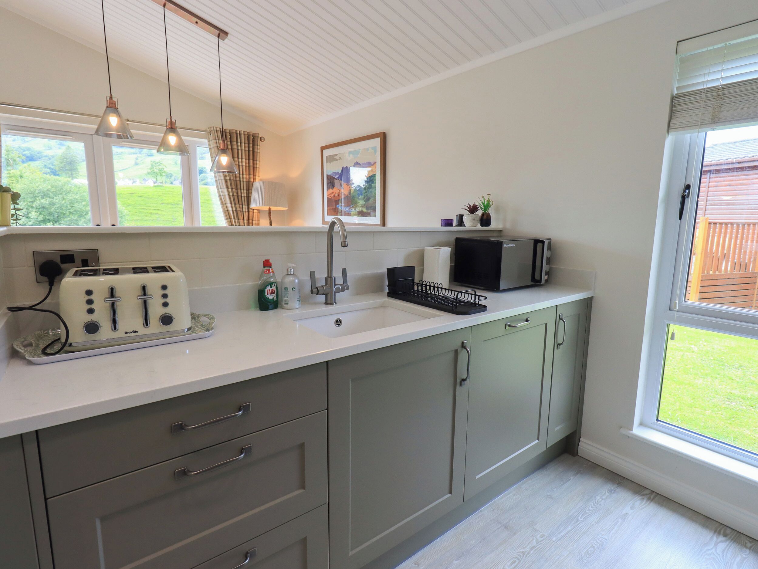 A modern kitchen with a white countertop, stainless steel appliances, and a window with a view of greenery.