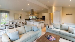 Ein modernes Wohnzimmer mit zwei Sofas, einem Couchtisch und einem Essbereich mit Stühlen und einem Tisch. Im Hintergrund ist eine Küche mit einer Kochinsel und Barhocker zu sehen.