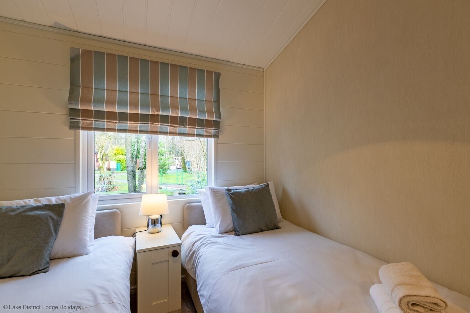 Une chambre avec deux lits, une table de chevet avec une lampe et une fenêtre donnant sur un paysage verdoyant.