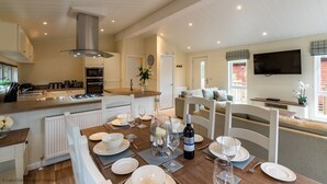 Eine helle, geräumige Küche mit modernen Geräten, ein Essbereich, der für eine Mahlzeit gedeckt ist, und ein gemütliches Wohnzimmer mit Fernseher.