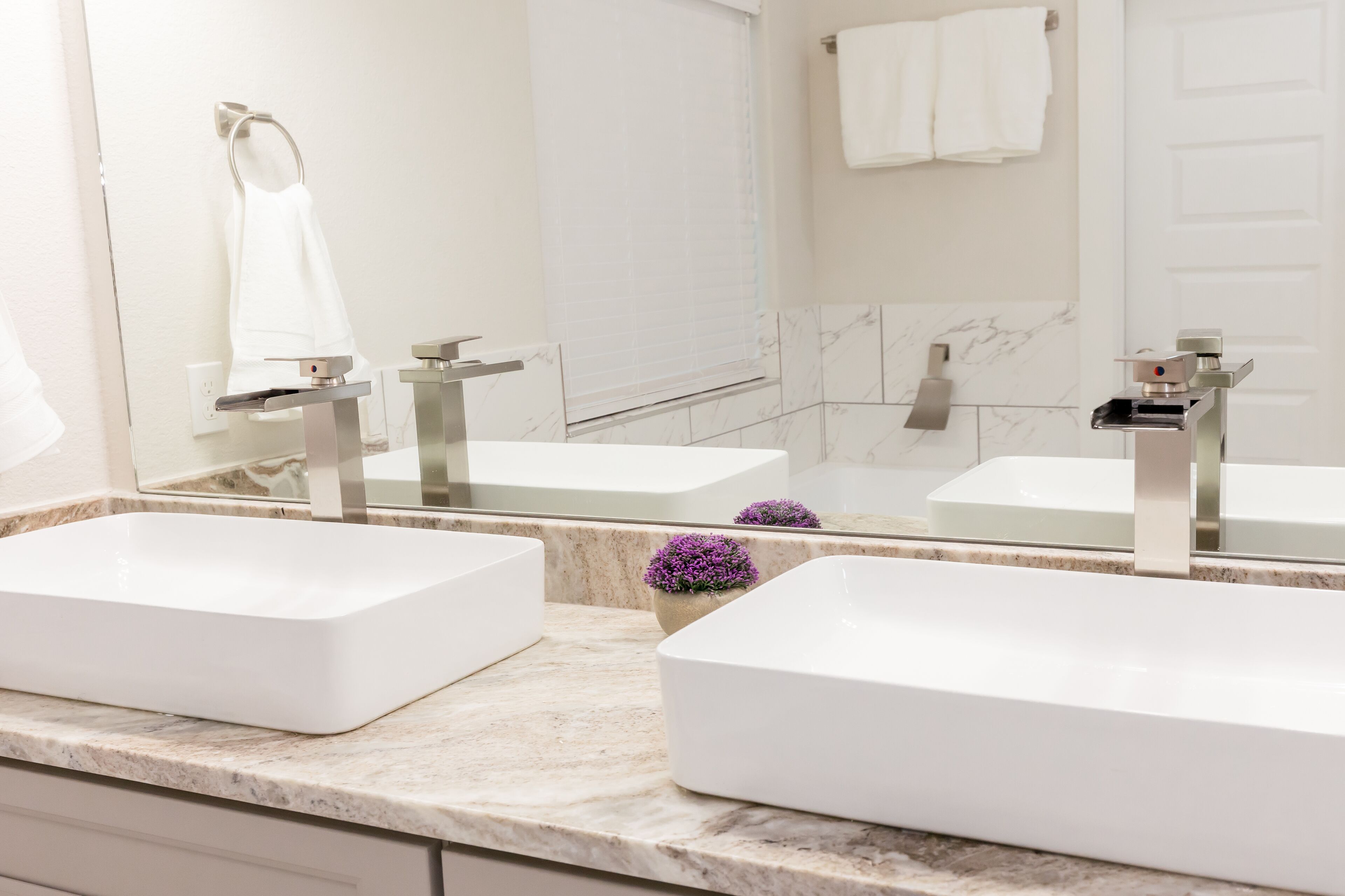 A bathroom with two white sinks, a mirror, a towel rack, and a potted plant.