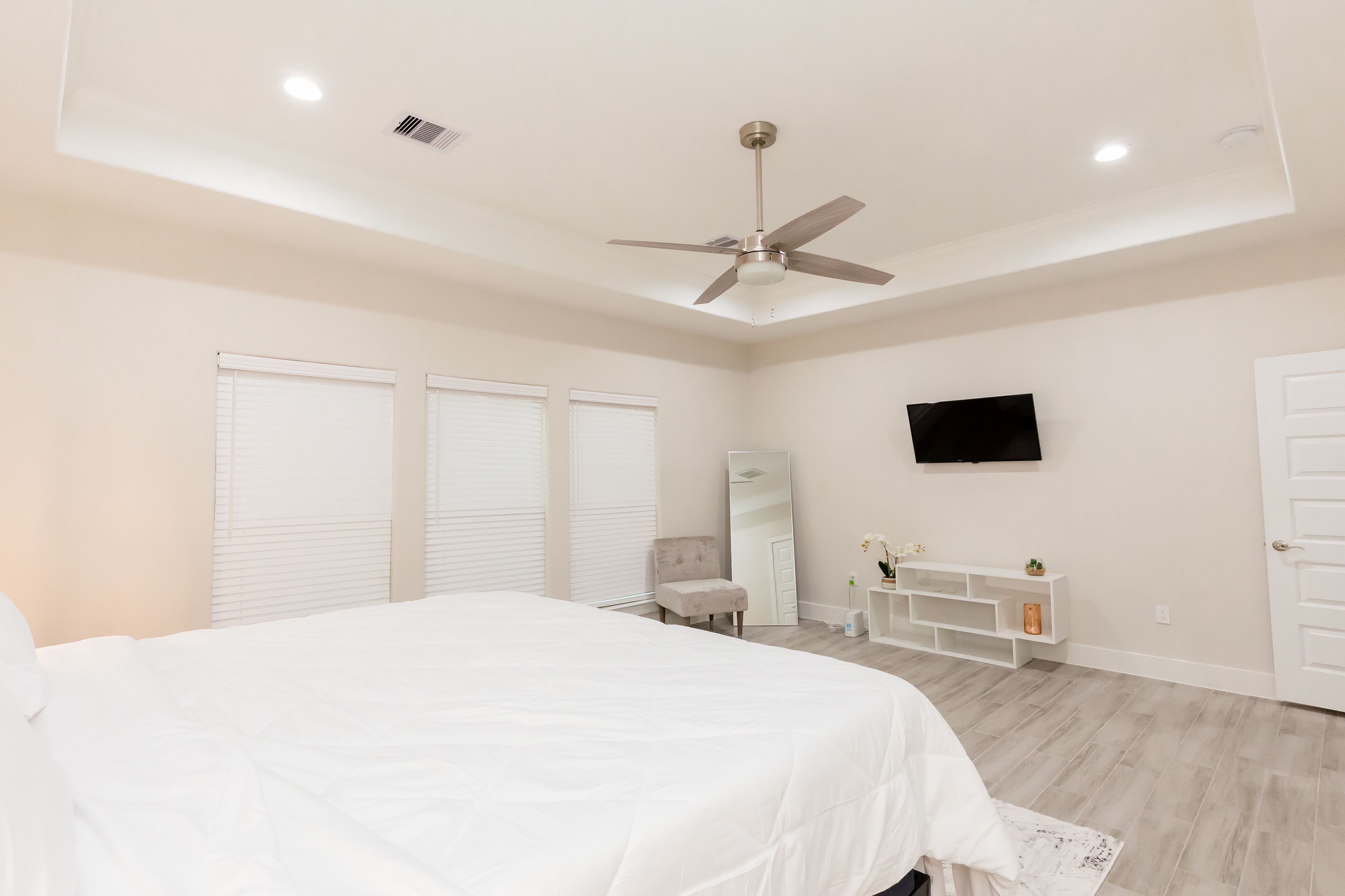 Une chambre à coucher comprenant un lit, un ventilateur de plafond, une télévision, une coiffeuse et une porte.